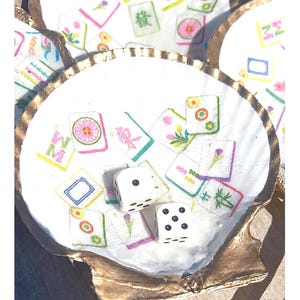 May include: White seashell with gold trim, filled with colorful Mahjong tiles and two white dice. The tiles feature floral and Chinese character designs. A unique decorative piece.
