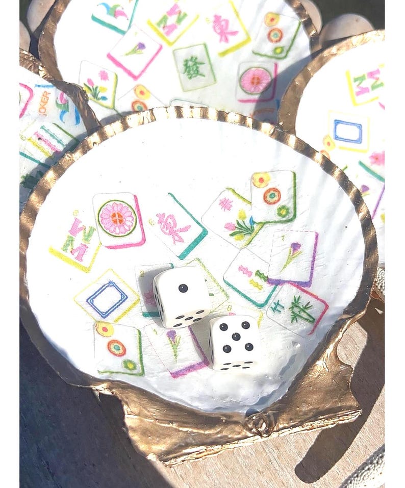 May include: White seashell with gold trim, filled with colorful Mahjong tiles and two white dice. The tiles feature floral and Chinese character designs. A unique decorative piece.
