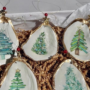 May include: Five oyster shell Christmas ornaments with gold trim and painted green Christmas trees. Each ornament has a red bead and gold star on top.