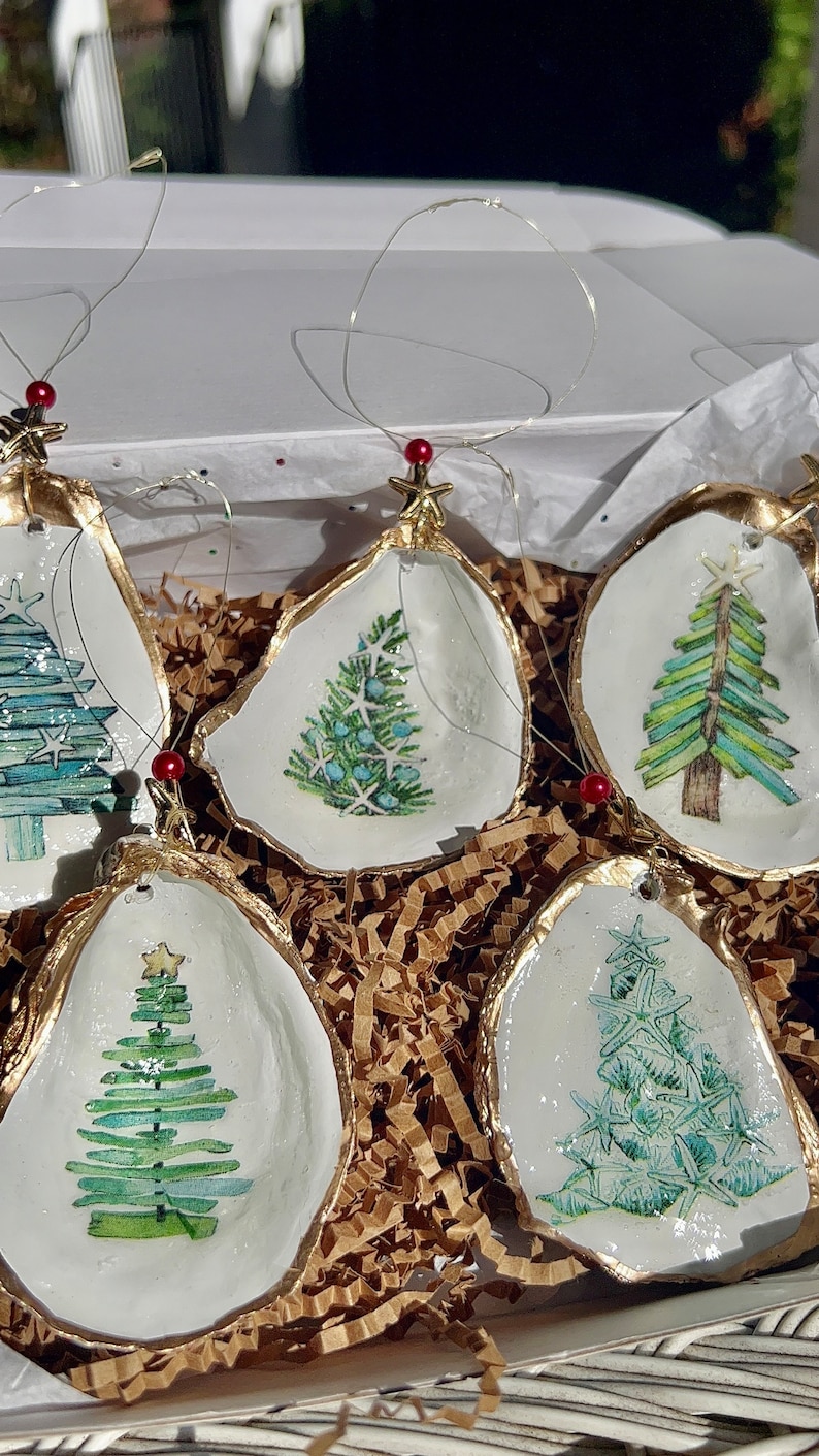 May include: Five oyster shell Christmas ornaments with gold trim and painted green Christmas trees. Each ornament has a red bead and gold star on top.
