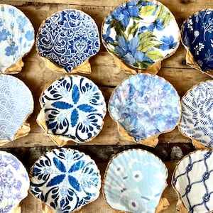 May include: Twelve scallop shells with gold edges, each decorated with a different blue and white patterned design.