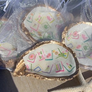 May include: Oyster shell trinket dishes with gold-painted edges, filled with colorful Mahjong tile designs. The shells are presented in sheer white organza bags, with a starfish in the foreground.