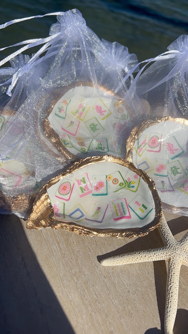 May include: Oyster shell trinket dishes with gold-painted edges, filled with colorful Mahjong tile designs. The shells are presented in sheer white organza bags, with a starfish in the foreground.