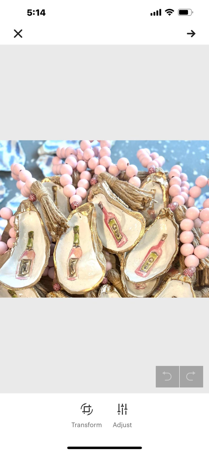 K&ouml;nnte beinhalten: Eine rosa Perlenkette mit goldbemalten Austernmuschel-Anh&auml;ngern. Jeder Anh&auml;nger zeigt ein handgemaltes Design einer Weinflasche.