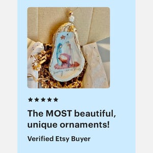 May include: A hand-painted Christmas ornament featuring the nativity scene, with the words "merry christmas" written on the bottom. The ornament is made from a natural oyster shell and is decorated with gold glitter.