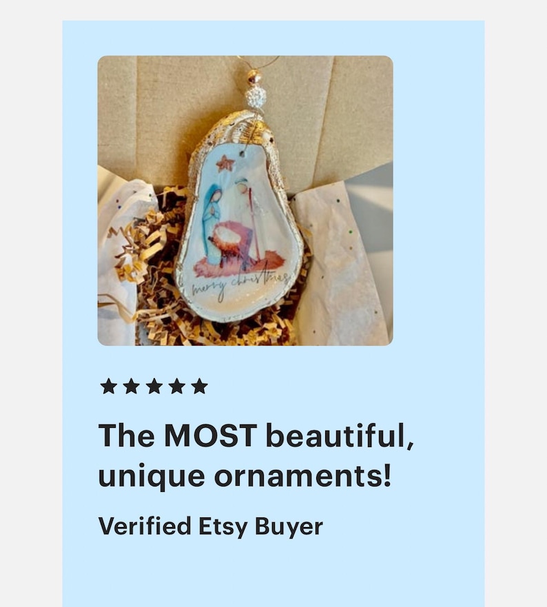 May include: A hand-painted Christmas ornament featuring the nativity scene, with the words "merry christmas" written on the bottom. The ornament is made from a natural oyster shell and is decorated with gold glitter.