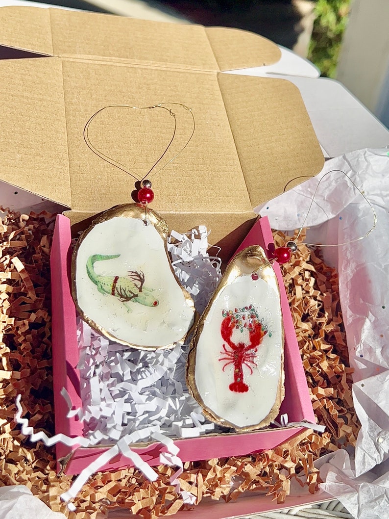May include: Two oyster shell Christmas ornaments, one with a green and white seahorse design and the other with a red lobster and holly design.