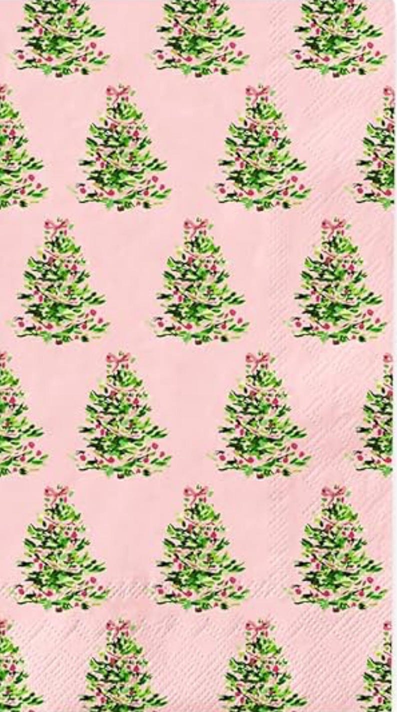 May include: Pink paper napkins with a repeating pattern of watercolor Christmas trees. Each tree is green with red ornaments and a pink bow at the top. The background is a solid light pink color.