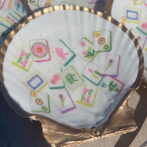 May include: White seashell-shaped dishes with gold-painted edges. Each dish is decorated with colorful Mahjong tiles. The tiles feature various symbols and characters, creating a unique decorative item.