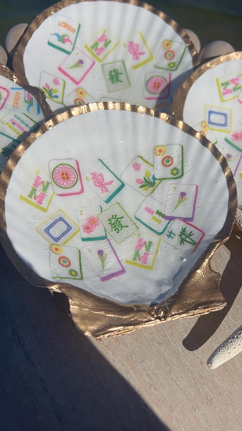 May include: White seashell-shaped dishes with gold-painted edges. Each dish is decorated with colorful Mahjong tiles. The tiles feature various symbols and characters, creating a unique decorative item.