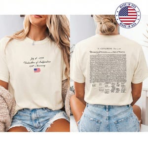 May include: Cream-coloured t-shirt with the text "July 4, 1776 Declaration of Independence 250th Anniversary" and an American flag graphic. The back of the shirt displays the text of the Declaration of Independence. A "Made in USA" logo is visible.