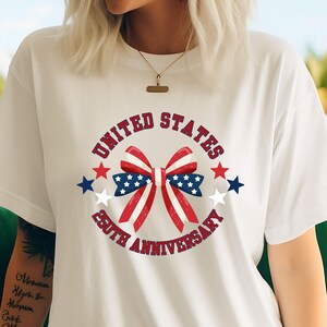 May include: White t-shirt featuring a patriotic design. The design includes a red, white, and blue bow with stars and the text "UNITED STATES 250TH ANNIVERSARY" in a circular arrangement. The shirt is a casual wear item.