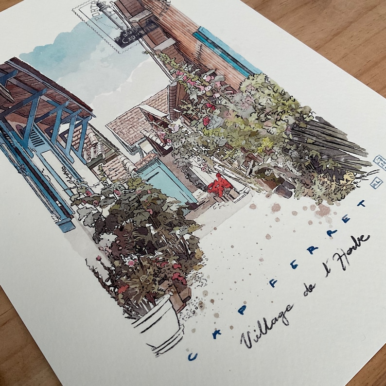 May include: Watercolor painting of a European village scene. The artwork depicts buildings with blue shutters and a red awning, with lush greenery and the text "CAP FERRET Village de l'Herbe".