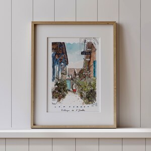 May include: Framed watercolor print of a village street scene. The artwork features buildings with blue accents, lush greenery, and the text "C.A.P. FERRET Village de l'Imbre". The print is in a gold frame.