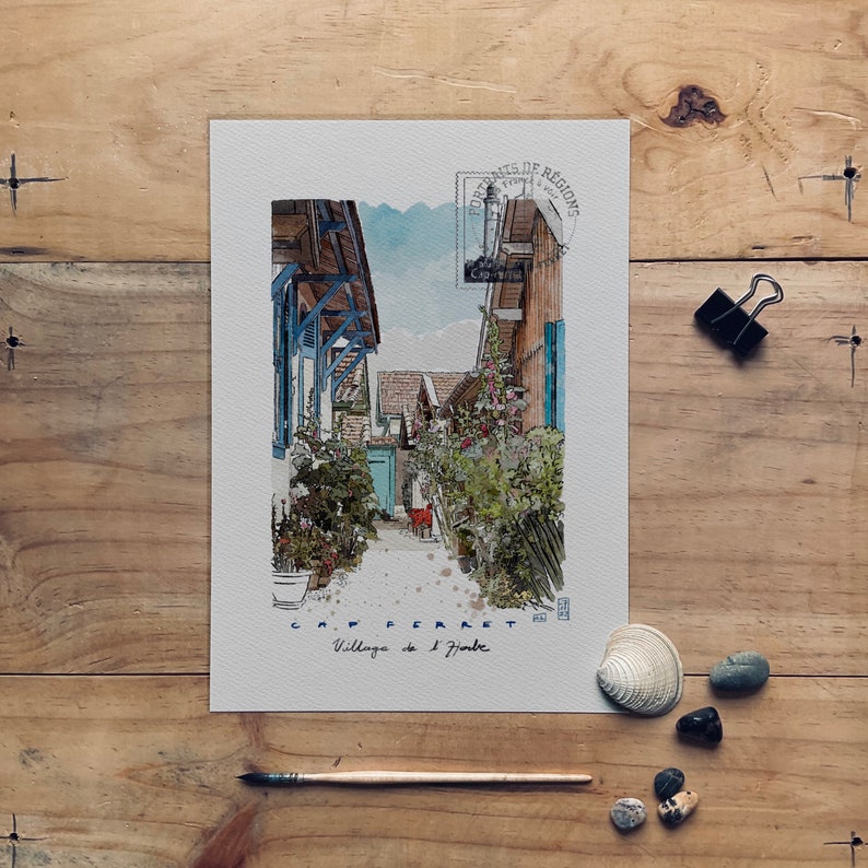 May include: Watercolor print of a village scene, featuring buildings with blue and brown accents, lush greenery, and a narrow pathway. The print includes text that reads "CAP FERRET Village de l'Herbe."