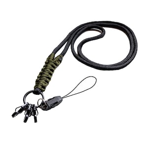 Puede incluir: Un cordón de paracord negro y verde con un clip de plástico negro y varios anillos metálicos.