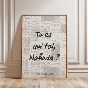 Op de afbeelding: Een ingelijst drukwerk met een krantenachtergrond en de tekst "Tu es qui toi, Nahuda?" in zwarte letters. Onderaan het drukwerk staat de tekst "Fabrice Les Anges".