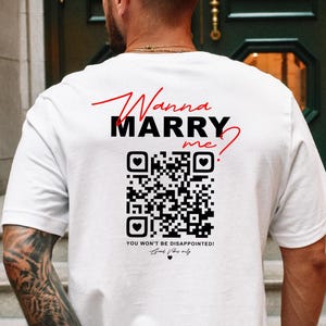 Könnte beinhalten: Weißes T-Shirt mit dem Text "Wanna MARRY me?" in Rot und Schwarz. Unter dem Text befindet sich ein QR-Code und die Worte "You won't be disappointed!" in Schwarz. Das T-Shirt wird von einer Person getragen.