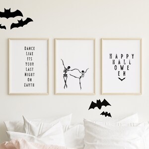 Może przedstawiać: Trzy czarno-białe oprawione wydruki z tekstem i obrazami o tematyce Halloween. Wydruki wiszą na białej ścianie z wycięciami czarnych nietoperzy. Tekst na wydrukach brzmi "Dance like it's your last night on earth", "Happy Halloween" i tańczący szkielet.