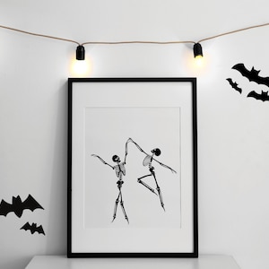 May include: Black framed print featuring a black and white illustration of two dancing skeletons. The skeletons are in a ballet pose. The background is white with black bat silhouettes and string lights.
