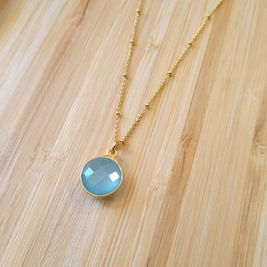 Colar com pingente de calcedônia azul e banho de ouro. Pingente com pedra natural facetada de 12 mm. Delicada corrente com detalhes em ouro.