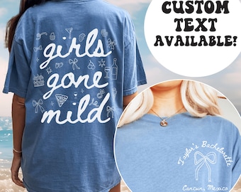 Puede incluir: Una camiseta azul claro con el texto "girls gone mild" en letras blancas y varias pequeñas ilustraciones blancas. La parte posterior de la camiseta tiene un lazo blanco y el texto "Taylor's Bachelorette Cancun, México".