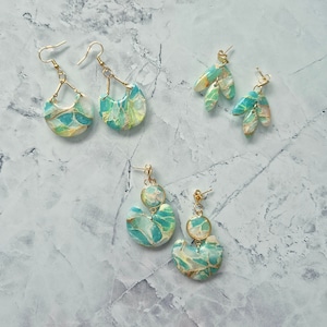 May include: Four pairs of earrings with gold accents and a marbled design in shades of green, white, and gold.