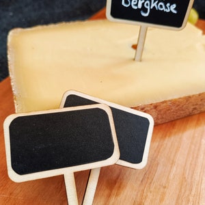 Könnte beinhalten: Ein Stück Käse mit zwei leeren Schiefertafeln und einem Schiefertafeln, auf dem "Bergkäse" steht.