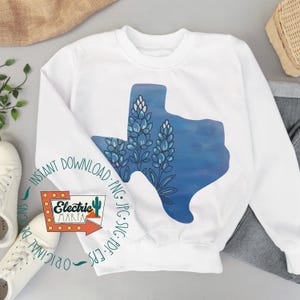 May include: White crewneck sweatshirt featuring a blue watercolor design of the state of Texas with bluebonnet flowers. The sweatshirt has the text "Instant Download" and "Electric Marta" on it. The design is a digital download.