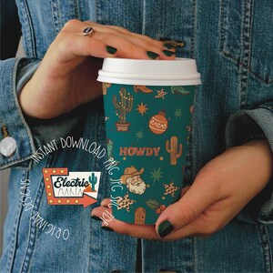 May include: A teal coffee cup with a white lid, featuring a repeating pattern of cacti, stars, and a cowboy Santa. The word "HOWDY" is printed on the cup. The cup is held by a person wearing a denim jacket. The logo for Electric Marfa is visible.