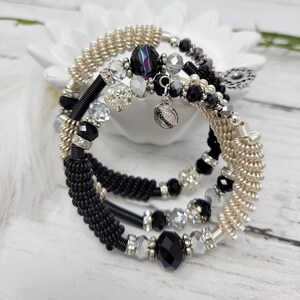 May include: A set of three bracelets featuring black and cream wire wrapped with black and clear beads, and a silver charm.