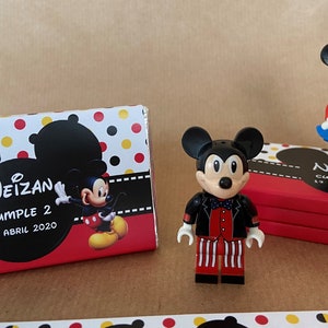 Könnte beinhalten: Zwei kleine Plastikfiguren von Mickey Mouse und Minnie Mouse. Mickey trägt eine rote Jacke, eine schwarze Fliege und eine weiß-rot gestreifte Hose. Minnie trägt ein rotes Shirt, eine blaue Latzhose und einen blauen Rock mit weißen Punkten. Die Figuren stehen auf einer rot-weißen Schachtel mit schwarzen Punkten und dem Text "Neizan Cumple 2 19 Abril 2020".