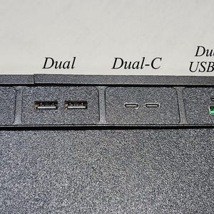 May include: A close-up of a black electronic device featuring various USB ports. The ports are labelled "Single", "Dual", "Dual-C", and "Dual USB+C". The "Dual USB+C" port has a green interior. The device has a textured surface.
