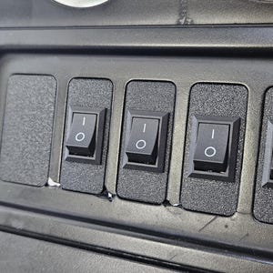 May include: A close-up of a black control panel with four rectangular toggle switches and a blank space. The switches have a white "O" and "I" symbol. The panel is set in a beige interior.