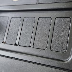 以下が含まれることがあります： 車の内装コンソールをクローズアップ。5つの長方形のボタンが付いた、質感のある黒いプラスチックパネル。左側には黒いマグネット式電話マウントがあり、ベージュの革のような素材がコンソールを縁取っています。