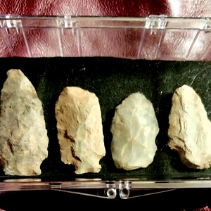 May include: A collection of five arrowheads displayed in a clear plastic case. The arrowheads are made of a light brown stone and have a variety of shapes and sizes.
