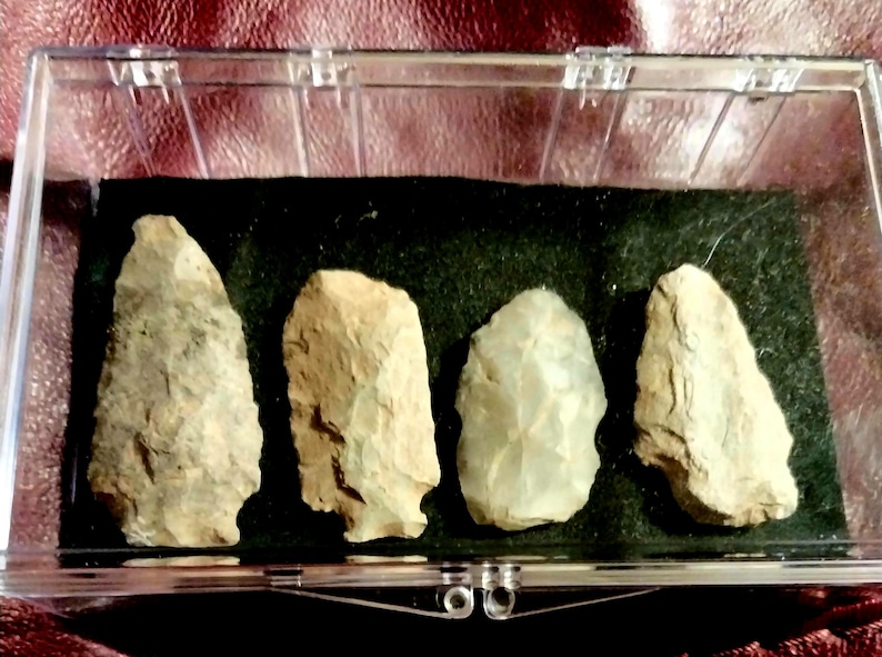May include: A collection of five arrowheads displayed in a clear plastic case. The arrowheads are made of a light brown stone and have a variety of shapes and sizes.