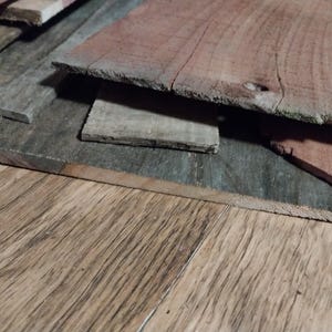 May include: A collection of weathered wooden planks in various shades of gray and reddish-brown. The planks are stacked, revealing their rough, textured surfaces and natural grain patterns. The image suggests a rustic or reclaimed wood theme.