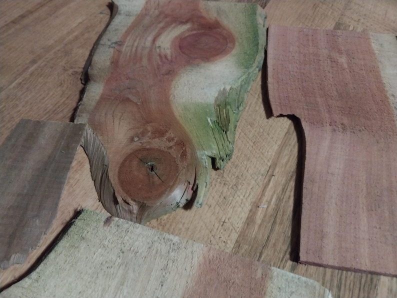 May include: Close-up of several irregularly shaped wood pieces. The wood features a variety of colors, including reddish-brown, green, and tan. The grain patterns are visible, with knots and natural edges. The pieces appear to be raw wood, possibly for crafting.