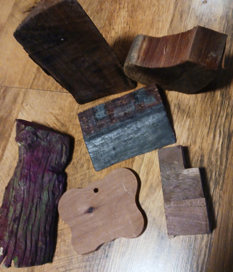 May include: Six pieces of wood in various shapes and sizes. The wood is a mix of dark brown, light brown, and purple. Some of the pieces have a rough, natural texture, while others are smooth. The wood is perfect for crafting projects.