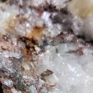 May include: Close-up of a rock formation with white, brown, and green crystals. The crystals are clustered together and have a rough, textured surface.