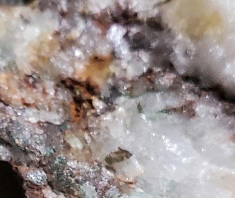 May include: Close-up of a rock formation with white, brown, and green crystals. The crystals are clustered together and have a rough, textured surface.