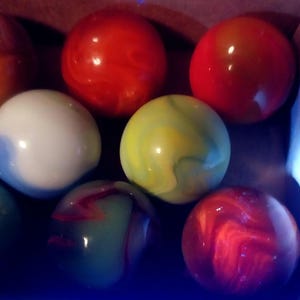 May include: A collection of colorful marbles in various colors, including red, white, green, and yellow. The marbles have a glossy finish and swirled patterns. The marbles are a classic toy.