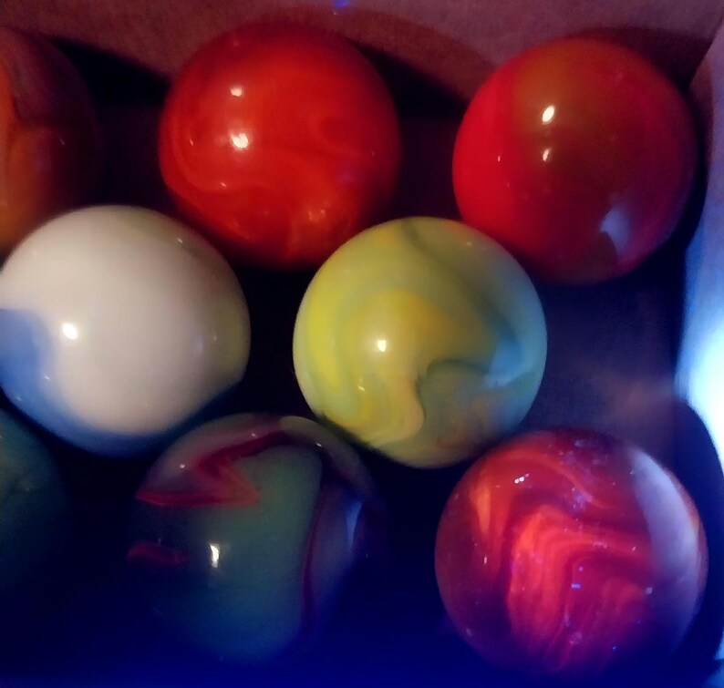May include: A collection of colorful marbles in various colors, including red, white, green, and yellow. The marbles have a glossy finish and swirled patterns. The marbles are a classic toy.