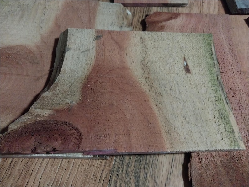May include: Close-up of several pieces of unfinished wood. The wood has a natural grain pattern with shades of red, brown, and tan. Some pieces have a curved edge. The wood appears to be ready for crafting or woodworking projects.