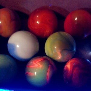 May include: A collection of colorful marbles in various shades of red, orange, green, white, and yellow. The marbles have a glossy finish and swirled patterns. The image is a close-up shot of the marbles.