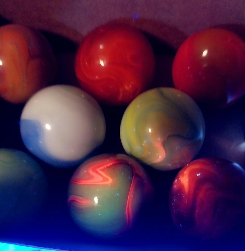 May include: A collection of colorful marbles in various shades of red, orange, green, white, and yellow. The marbles have a glossy finish and swirled patterns. The image is a close-up shot of the marbles.