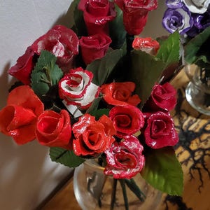 May include: A bouquet of red, white, and black roses in a clear glass vase. The roses are made of wood and have been painted.