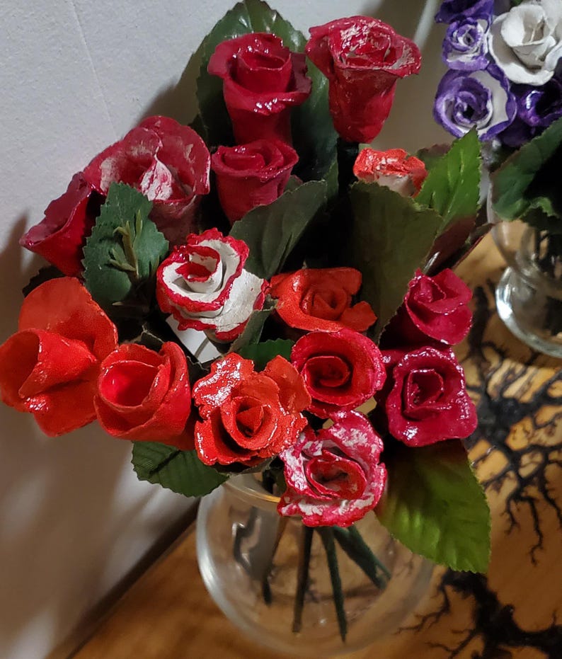 May include: A bouquet of red, white, and black roses in a clear glass vase. The roses are made of wood and have been painted.