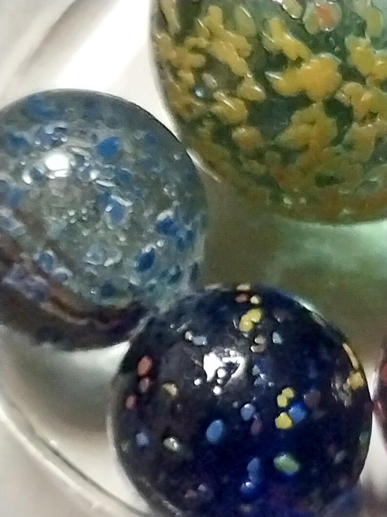 Op de afbeelding: Drie glazen knikkers met kleurrijke stippen. De knikkers zijn blauw, groen en zwart met gele, witte en rode stippen.